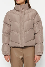 Person wearing a beige puffer jacket and pants on a white background