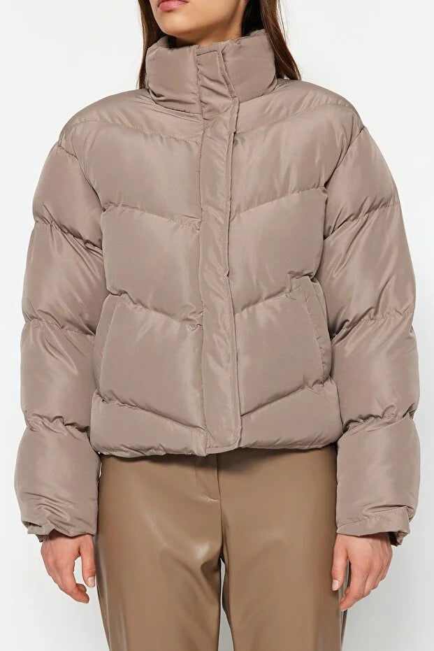 Person wearing a beige puffer jacket and pants on a white background