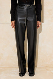 Person wearing black leather pants against a beige wall