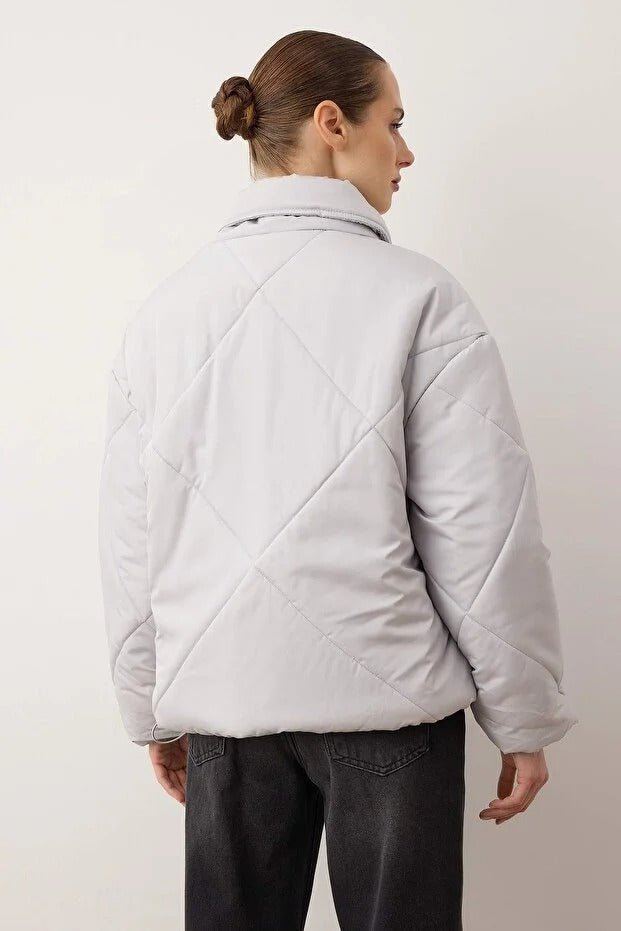 Person wearing a light gray quilted jacket against a plain background