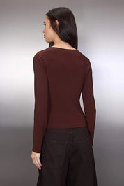 Woman wearing a brown long-sleeve top and dark pants against a plain background