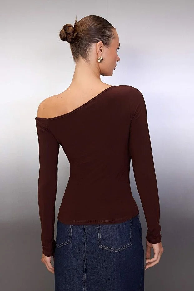 Woman wearing a brown one-shoulder top and blue jeans against a plain background