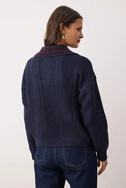 Person wearing a dark blue cable knit sweater with a white background