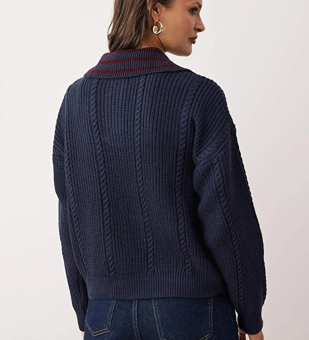 Person wearing a dark blue cable knit sweater with a white background