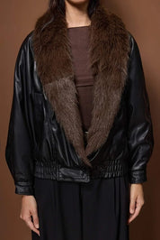 Person wearing a black leather jacket with a fur collar against a brown background