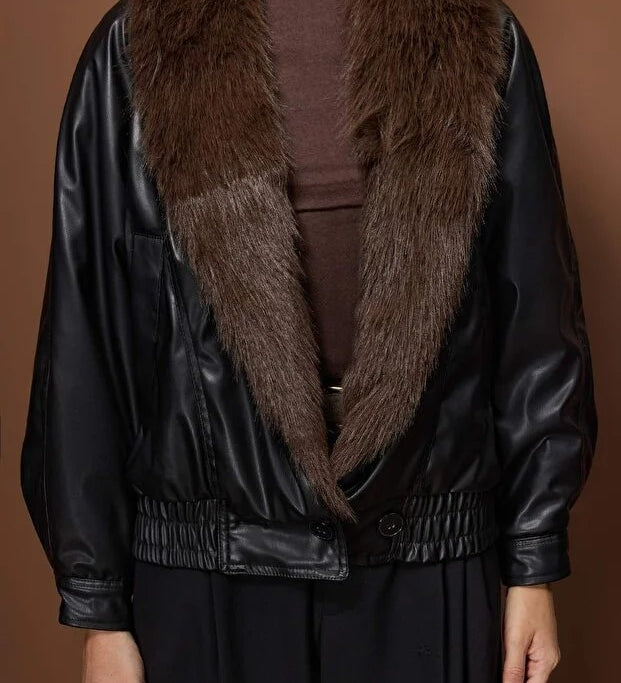 Person wearing a black leather jacket with a fur collar against a brown background