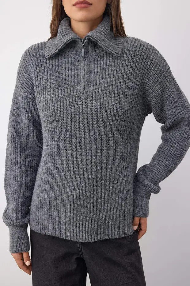 Person wearing a gray ribbed sweater against a white background