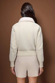 Person wearing a cream-colored outfit against a brown background