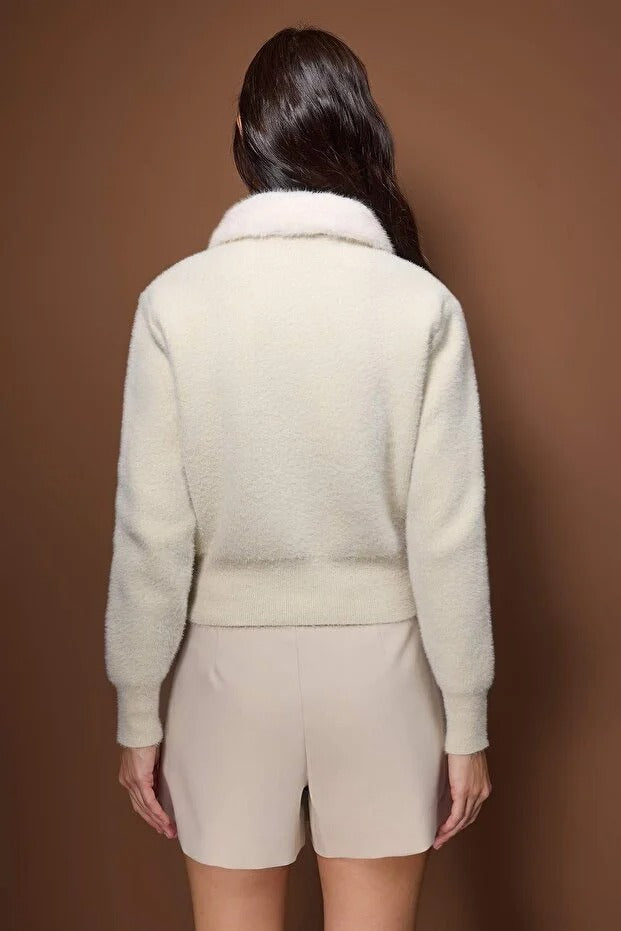 Person wearing a cream-colored outfit against a brown background