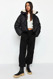 Person wearing a black puffer jacket with white lining on a white background