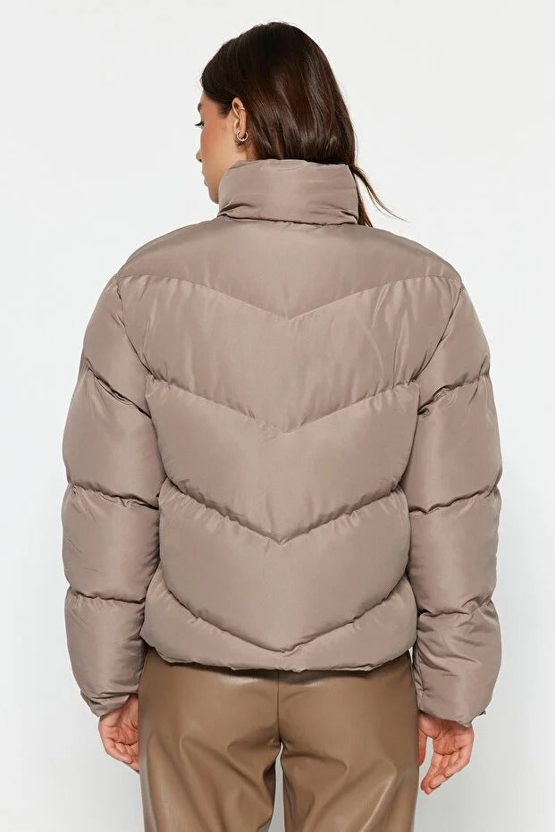 Person wearing a beige puffer jacket on a white background