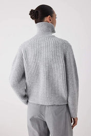 Person wearing a light gray ribbed sweater and pants on a white background