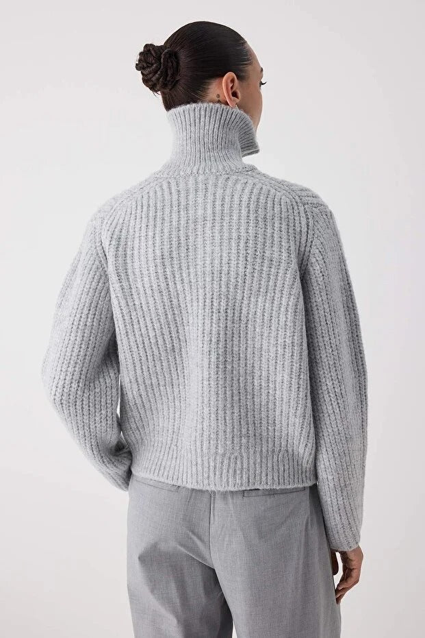Person wearing a light gray ribbed sweater and pants on a white background