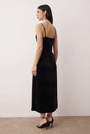 Woman wearing a black slip dress with thin straps against a plain background
