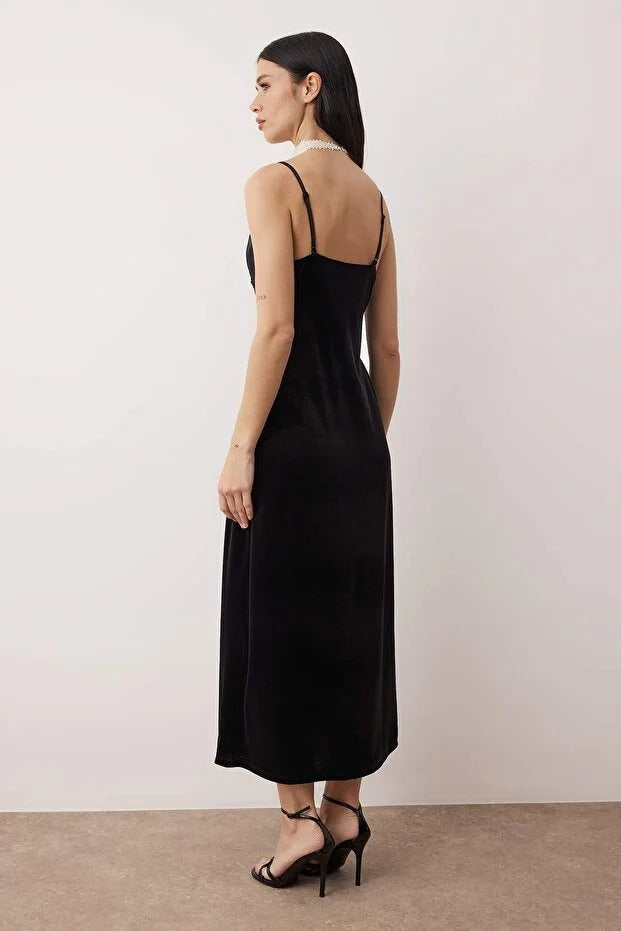 Woman wearing a black slip dress with thin straps against a plain background