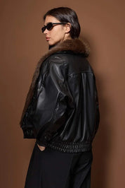 Person wearing a black leather jacket with fur collar against a brown background