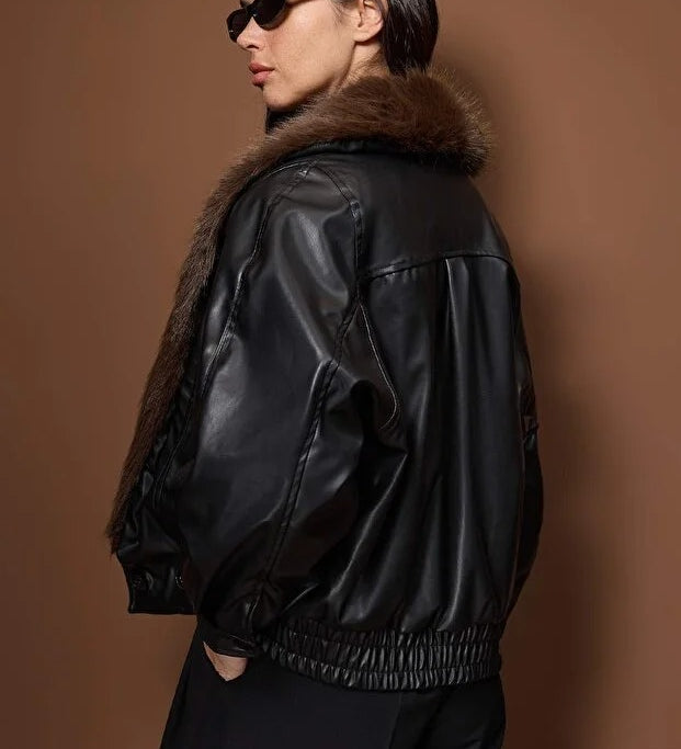 Person wearing a black leather jacket with fur collar against a brown background