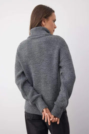 Person wearing a gray knitted sweater against a white background