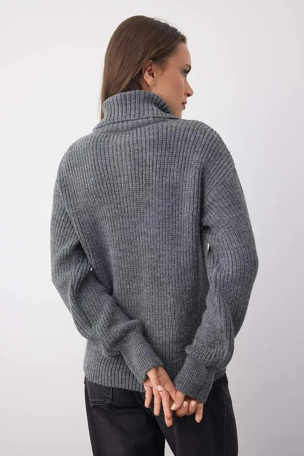 Person wearing a gray knitted sweater against a white background